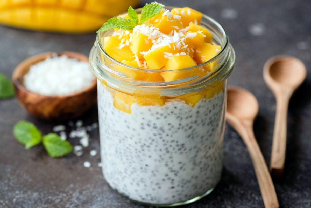 Pudim de chia com cubos de manga, coco ralado e hortelã em um pote de vidro